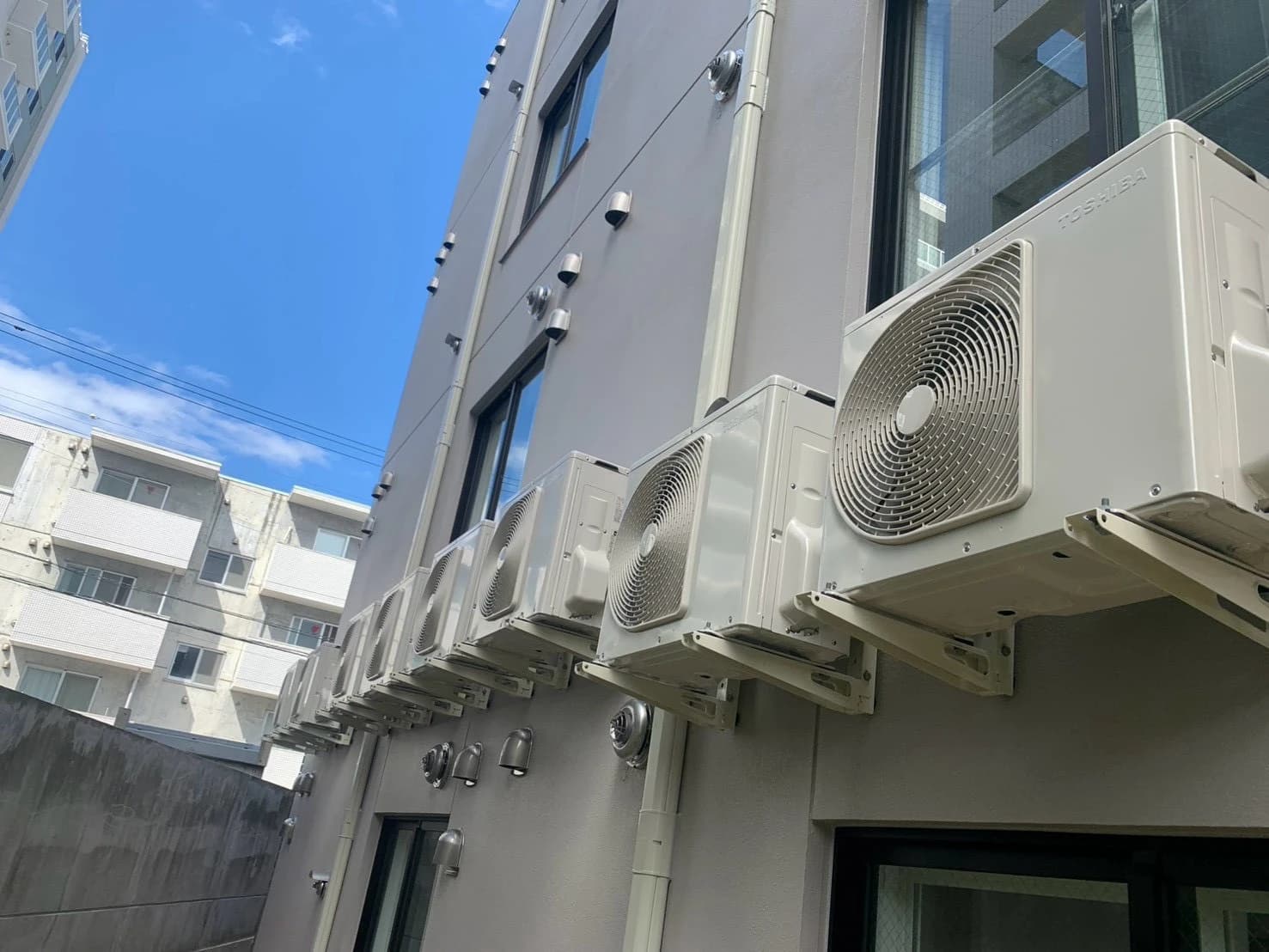 青空を背景に、マンション外壁へ整然と並べて設置した室外機の列