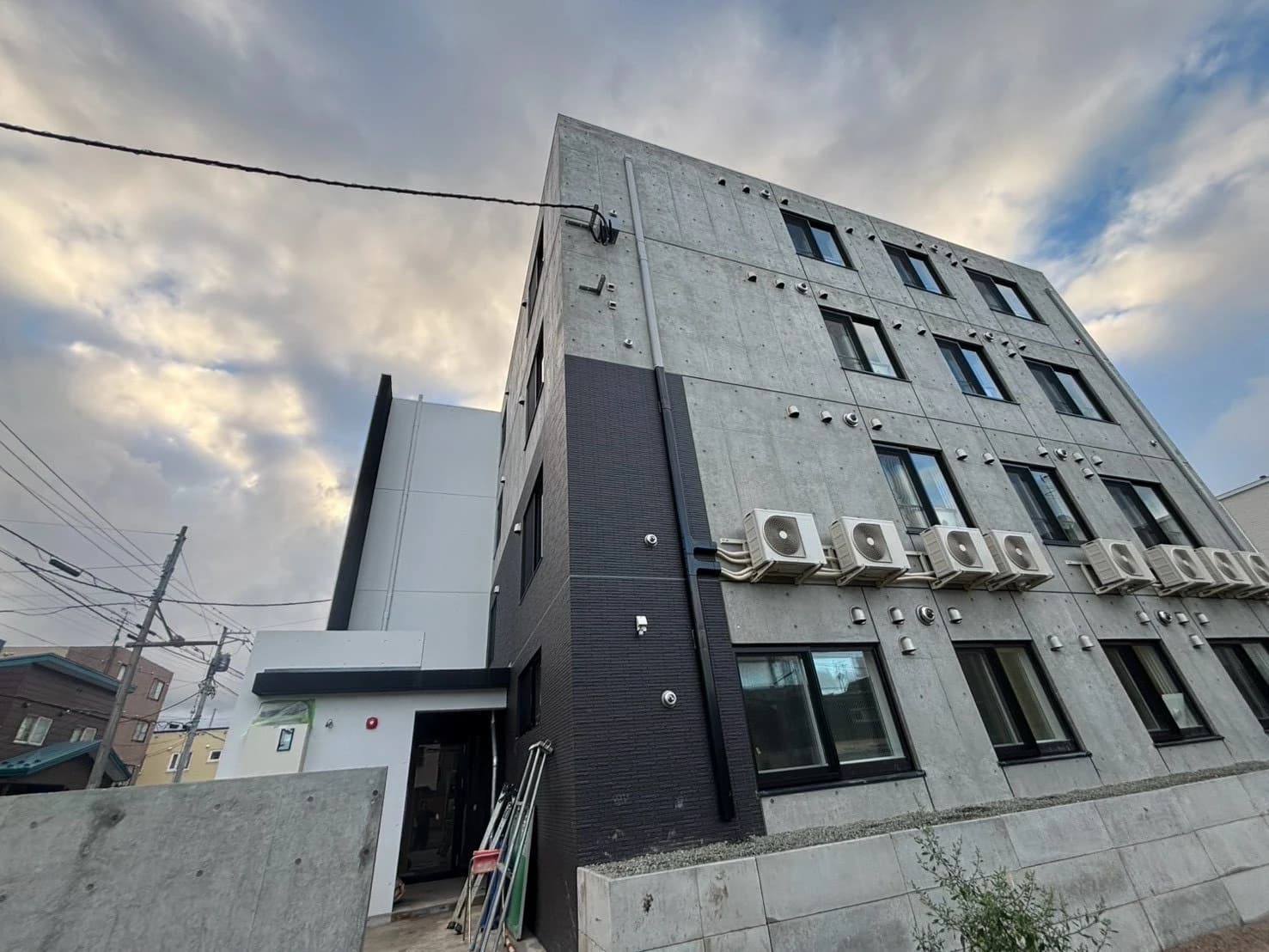 新築マンションの外壁に横一列に壁掛けで連装したエアコン室外機。コンクリート打放しの建物全景