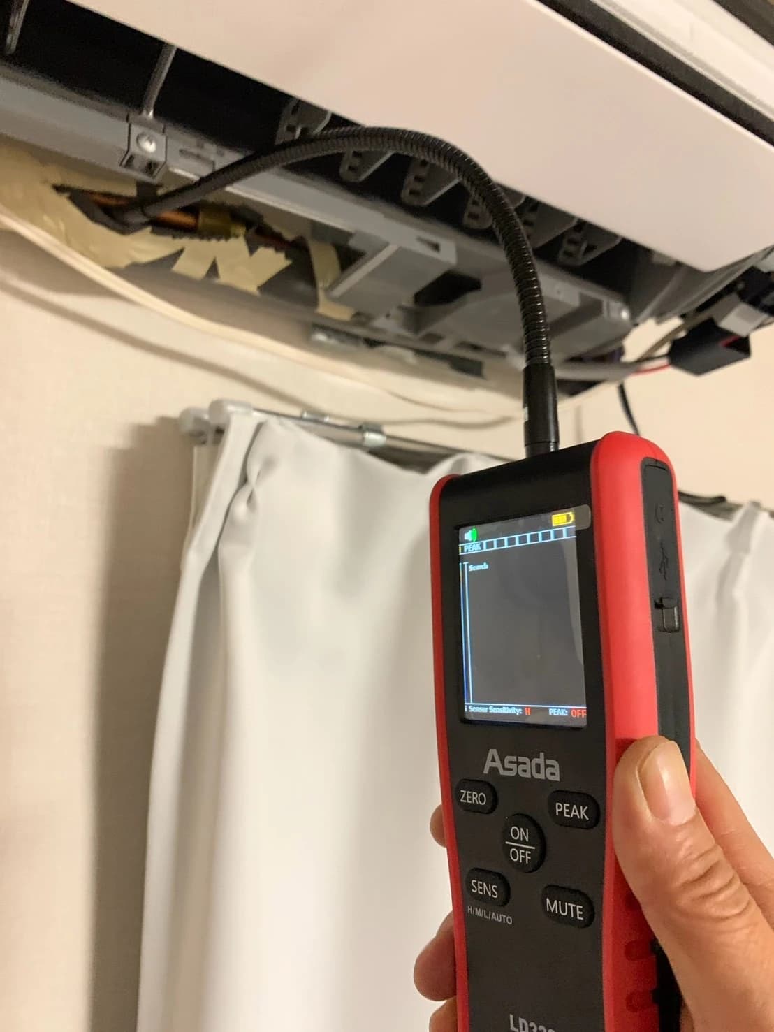室内機のカバーを開け、冷媒漏れ検知器のセンサーを配管接続部に当てて検査している様子