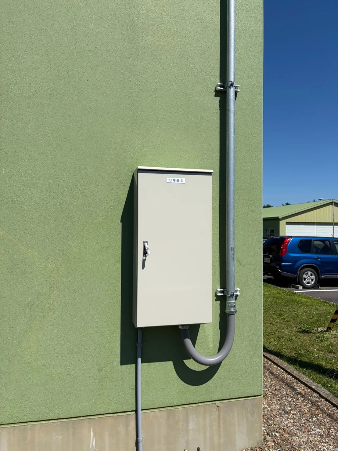 建物の外壁に設置した屋外用分電盤と、引込ポールからの電線管